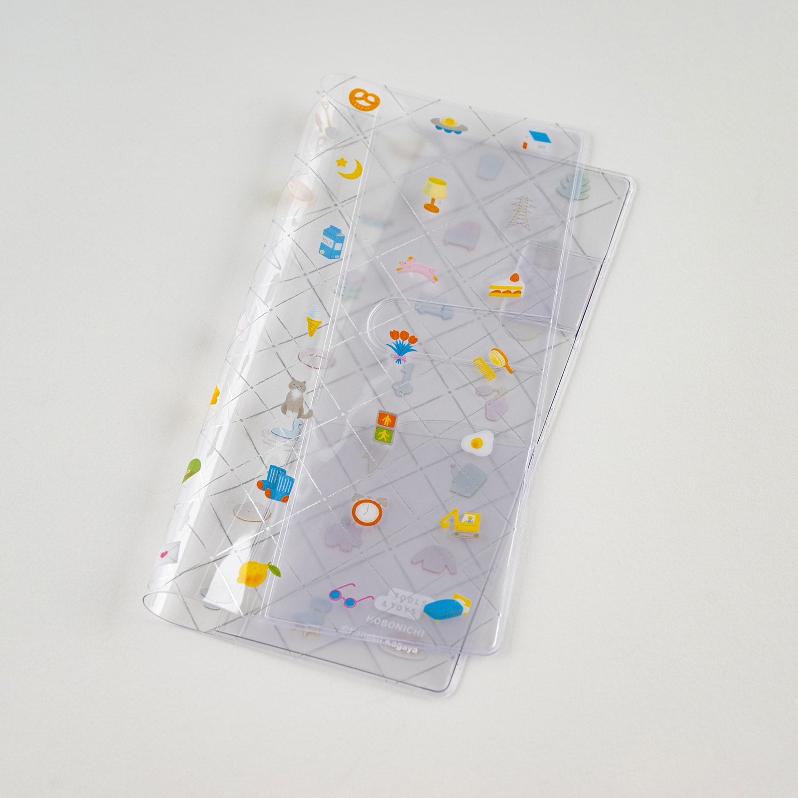 Hobonichi Kanako Kagaya: Clear Cover for Weeks (Familiar Sights) This is a protective cover that can be used on top of your Hobonichi Weeks to protect it from wear and tear. You can also store illustrations under your cover on cover to boost your Hobonichi covers design. This Weeks cover on cover also has a pen loop. The design for “Familiar Sights” was created by designer and illustrator Kanako Kagaya.